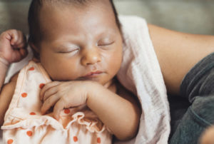 A baby sleeping peacefully in the arms of a caregiver.