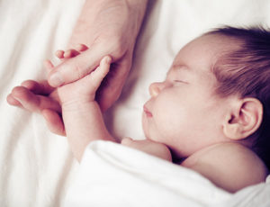 A parent holds their sleeping baby's hand.