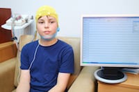 A child wearing an EEG cap while sitting next to a monitor displaying brain activity.