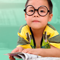Image of a child wearing glasses and reading a book.