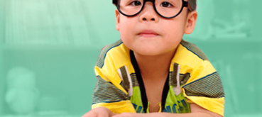 Image of a child wearing glasses and reading a book.