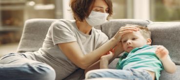 A woman with a face mask rests her palm on a child's head