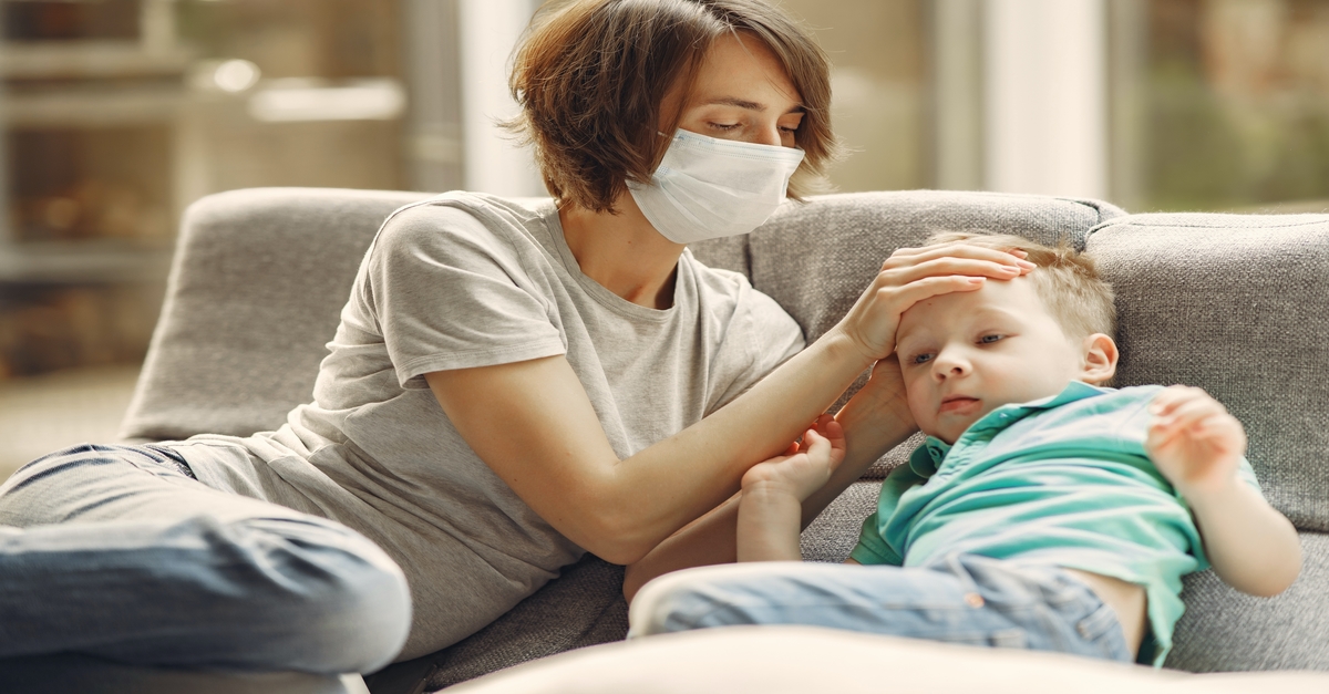 A woman with a face mask rests her palm on a child's head