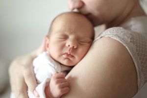 A mother holding her sleeping newborn close and kissing the baby's head.