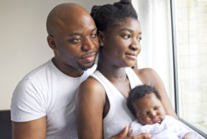 A couple holds their sleeping baby as they look out the window in content.