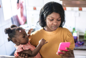 A young mother multitasking, holding her toddler in one arm while using her smartphone with the other hand.