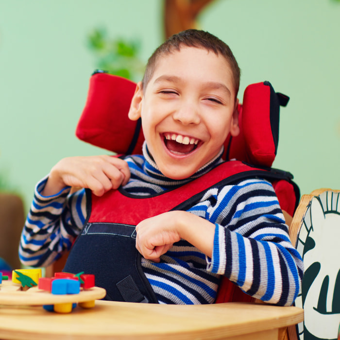 A boy with cerebral palsy sits at a desk smiling.
