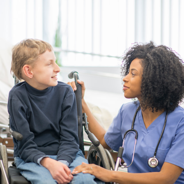 A nurse sits with a boy who has cerebral palsy.