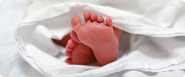 A newborn baby's feet stick out from under a blanket.