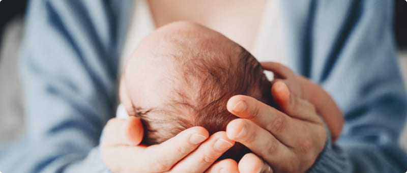 A health care provider cradles a newborn's head in their hands.