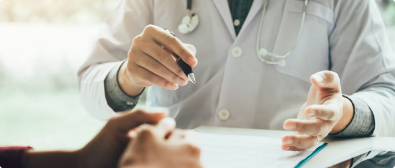 A doctor with a clipboard and pen explains a medical situation to their patient while sitting at a desk.