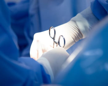 Doctors wearing surgical gloves and using forceps for a medical procedure. 