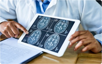 A doctor holding a tablet that displays brain scans, pointing to areas that may show signs of injury.