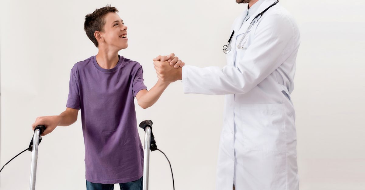 A child using a walker laughs and shakes hands with his doctor.