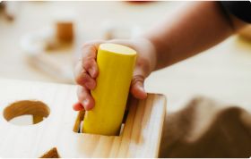 A child tries to fit a yellow round peg into a square hole on a wooden toy designed to help spot developmental delays.