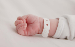 A close-up of a newborn's hand with a hospital ID wristband.