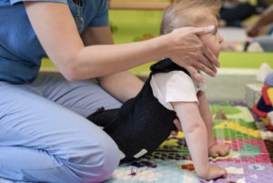 A therapist assisting a baby wearing a supportive vest during a physical therapy session.
