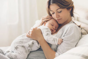A mother holding her sleeping baby close while resting in bed.