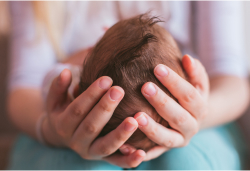 A caregiver gently cradling the back of a newborn's head with both hands.