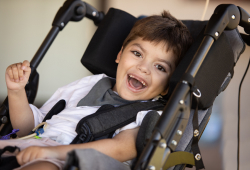 A young child with cerebral palsy smiling while seated in a supportive wheelchair.