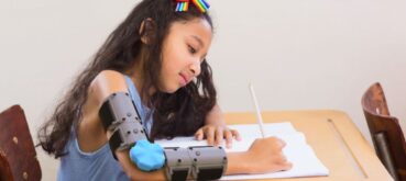 A young girl writes with the help of the Move-D cerebral palsy brace