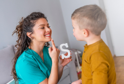 A speech therapist works with a young boy, holding a letter S to help with pronunciation.