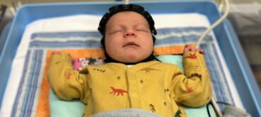 An infant rests in a cot and wears a cap designed to help with an early diagnosis of cerebral palsy and other birth injuries