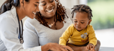 A doctor, parent, and young child look at a tablet during a medical appointment.