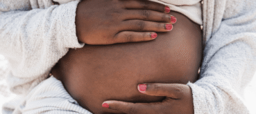 A pregnant person rests both hands on their belly.