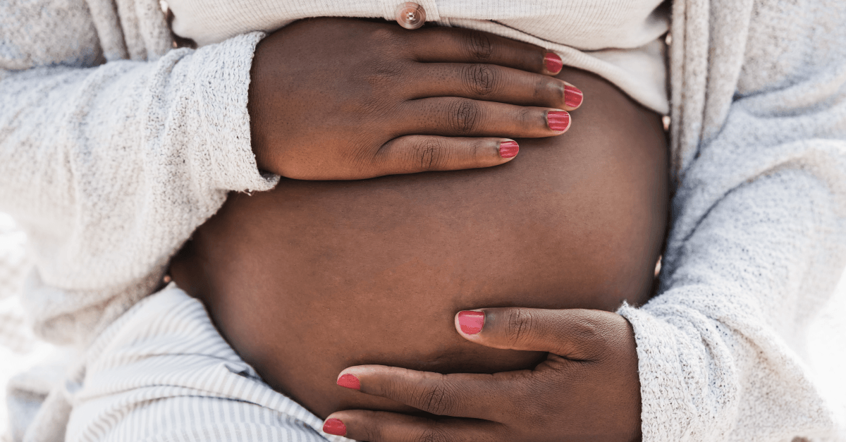 A pregnant person rests both hands on their belly.