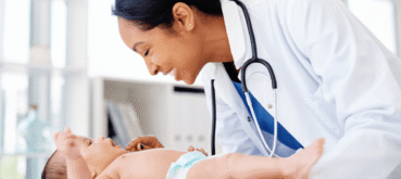 A doctor smiles while examining a baby during a medical checkup.