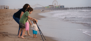 A family walks along the beach with a young child using forearm crutches.