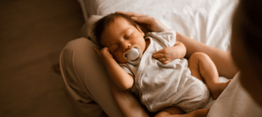 A sleeping baby with a pacifier rests in their mother's lap.