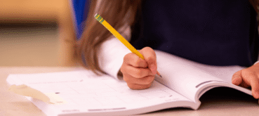 A student writes with a pencil in an open workbook.