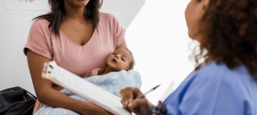 A mother holds her baby while talking with a health care provider.