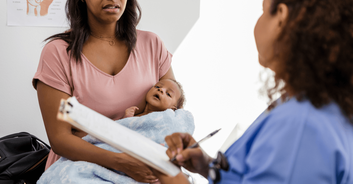A mother holds her baby while talking with a health care provider.